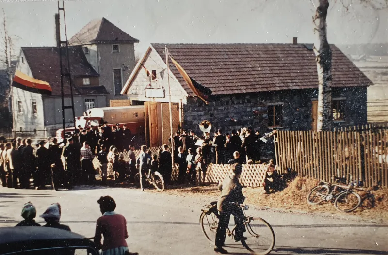 Farbfoto: Menschenmenge mit Fahnen und Musikkapelle vor dem Depot
