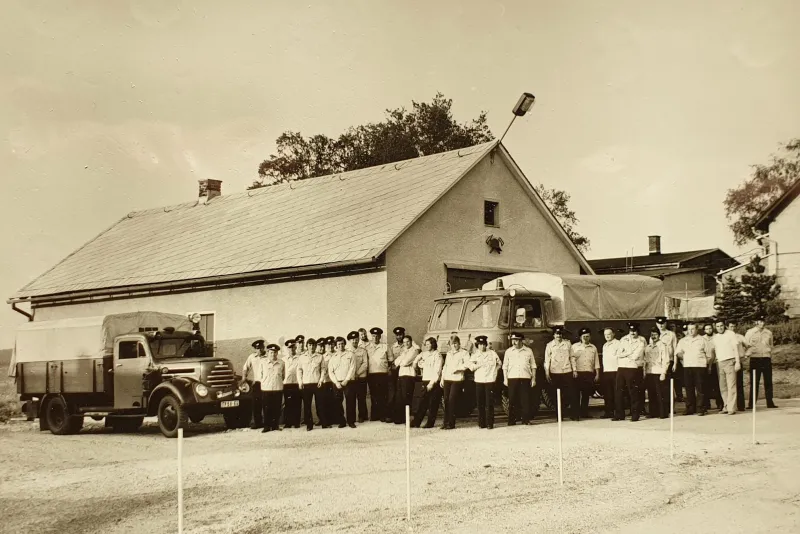Sepia-Foto: rund 30 Feuerwehrleute stehen in einer Reihe vor dem Depot, links und rechts je ein Lastwagen