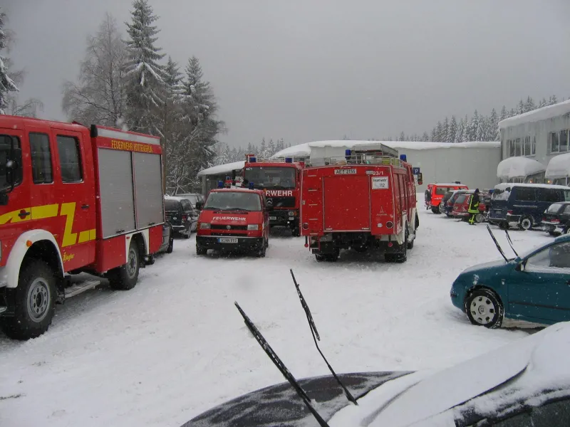 Farbfoto: Löschfahrzeuge mehrerer Feuerwehren auf einem verschneiten Parkplatz vor tief verschneiten Hallen