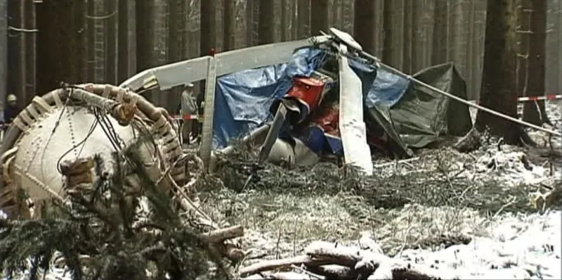 Farbfoto: Wrack eines Hubschraubers zwischen Fichten im verschneiten Wald, abgesperrt mit Flatterband