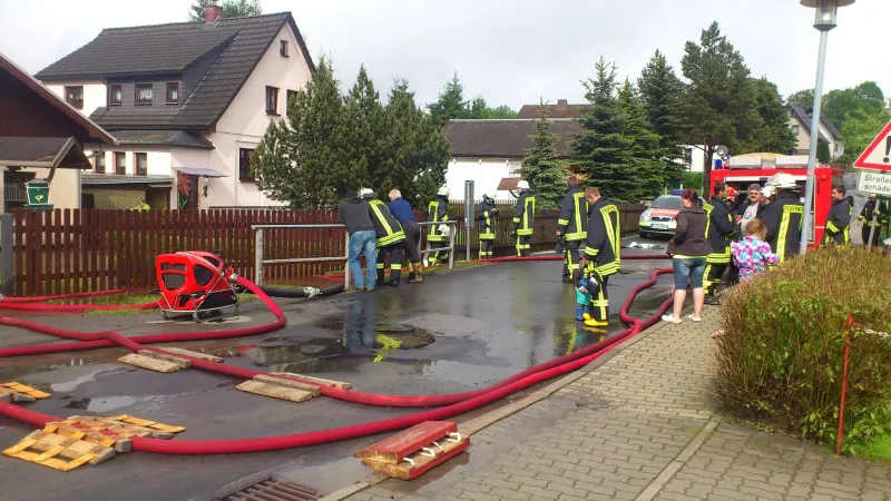 Farbfoto: Schlauchleitungen und eine Tragkraftspritze auf einer nassen Straße, dazwischen Einsatzkräfte